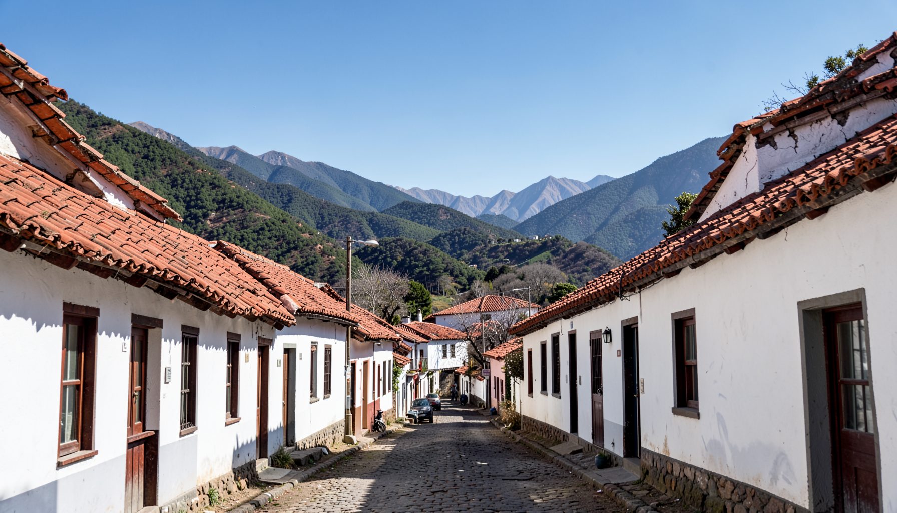 Vista de una calle en un pueblo andino con casas de fachadas blancas y techos de teja roja, rodeado de montañas verdes bajo un cielo despejado