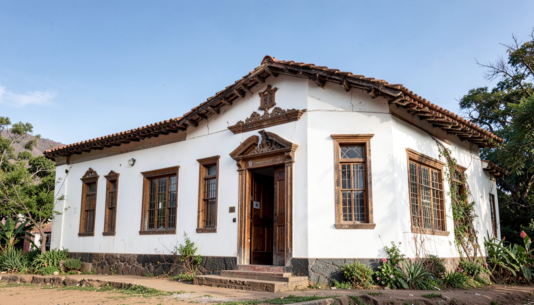 Edificio municipal de estilo colonial con fachada blanca y detalles en madera, bajo un cielo despejado de tonos azul suave, rodeado de vegetación andina.